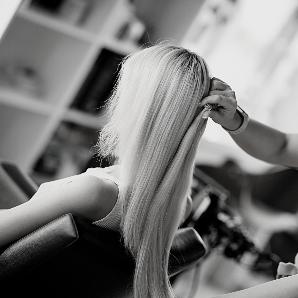 hair extensions blonde fusion bundle held up to blonde bridal hair client sitting in hair salon chair