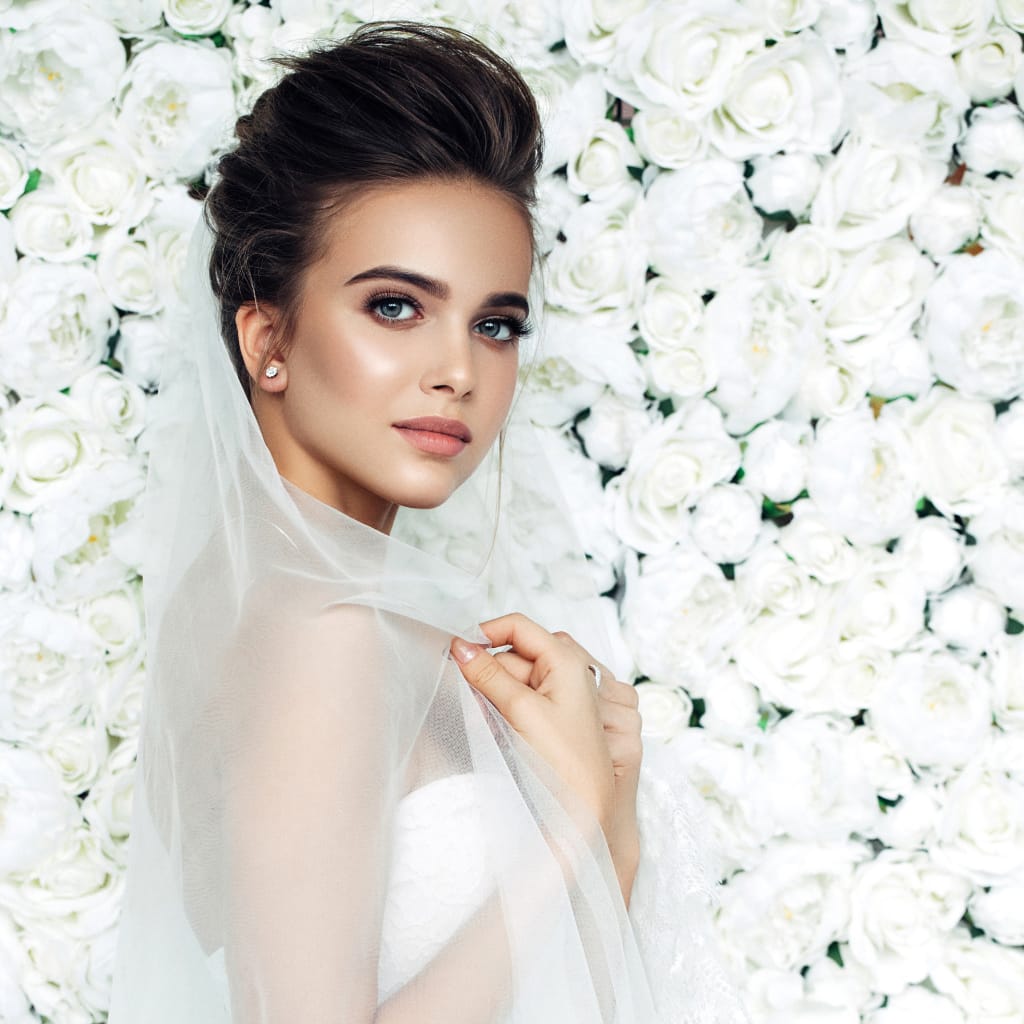 wedding hair updo long bridal veil covering shoulders bride in front of white rose wedding flower wall