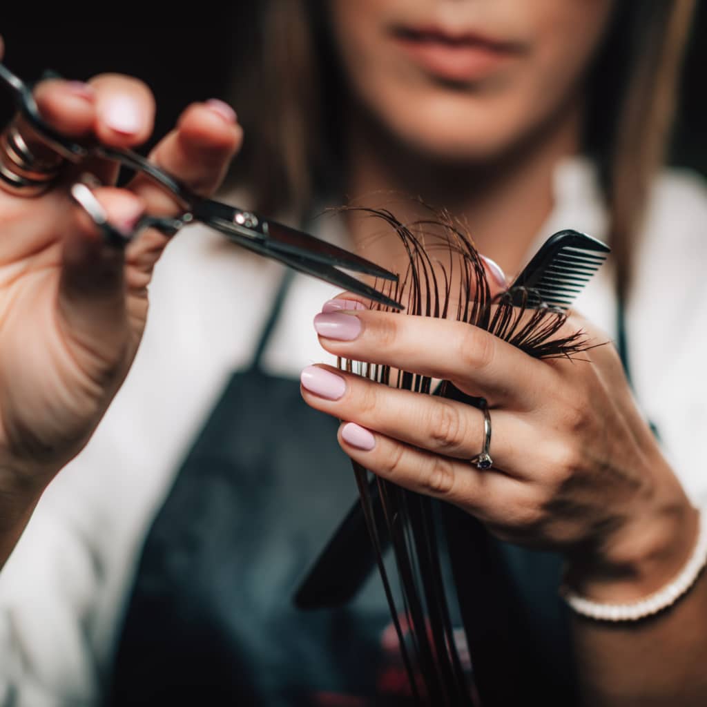 hair combed straight between mobile hairstylist fingers holding hair cutting shears in other hand