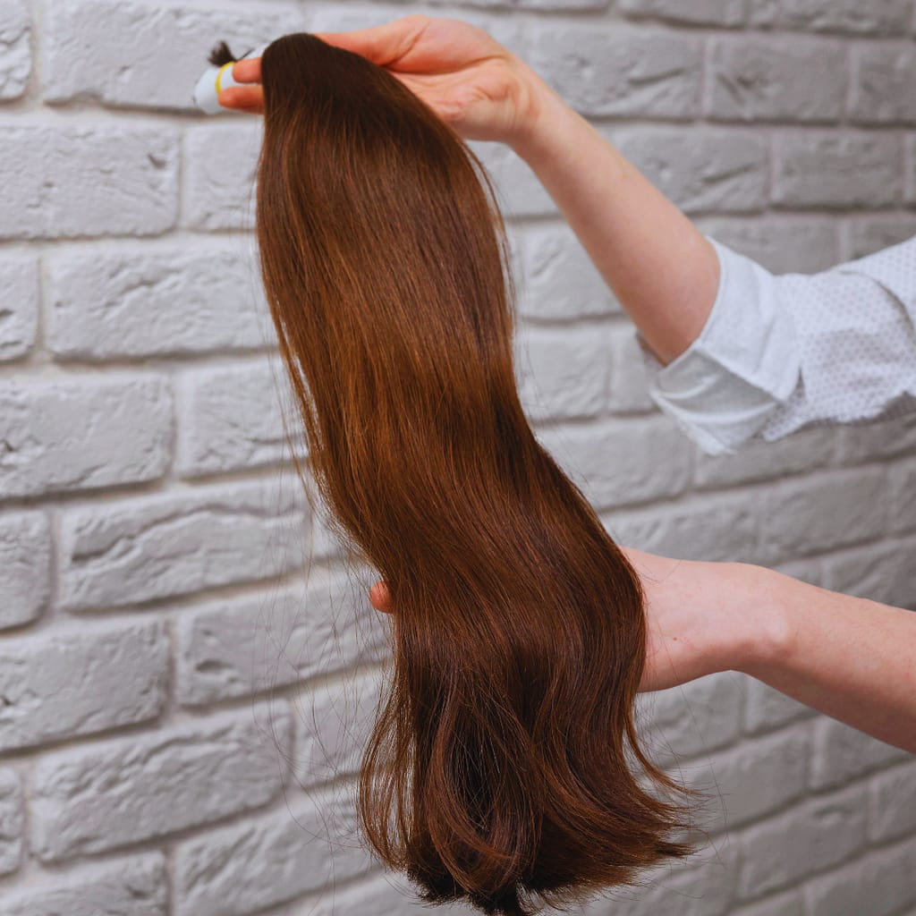 a hand showing a bundle of brunette hand tied weft hair extensions