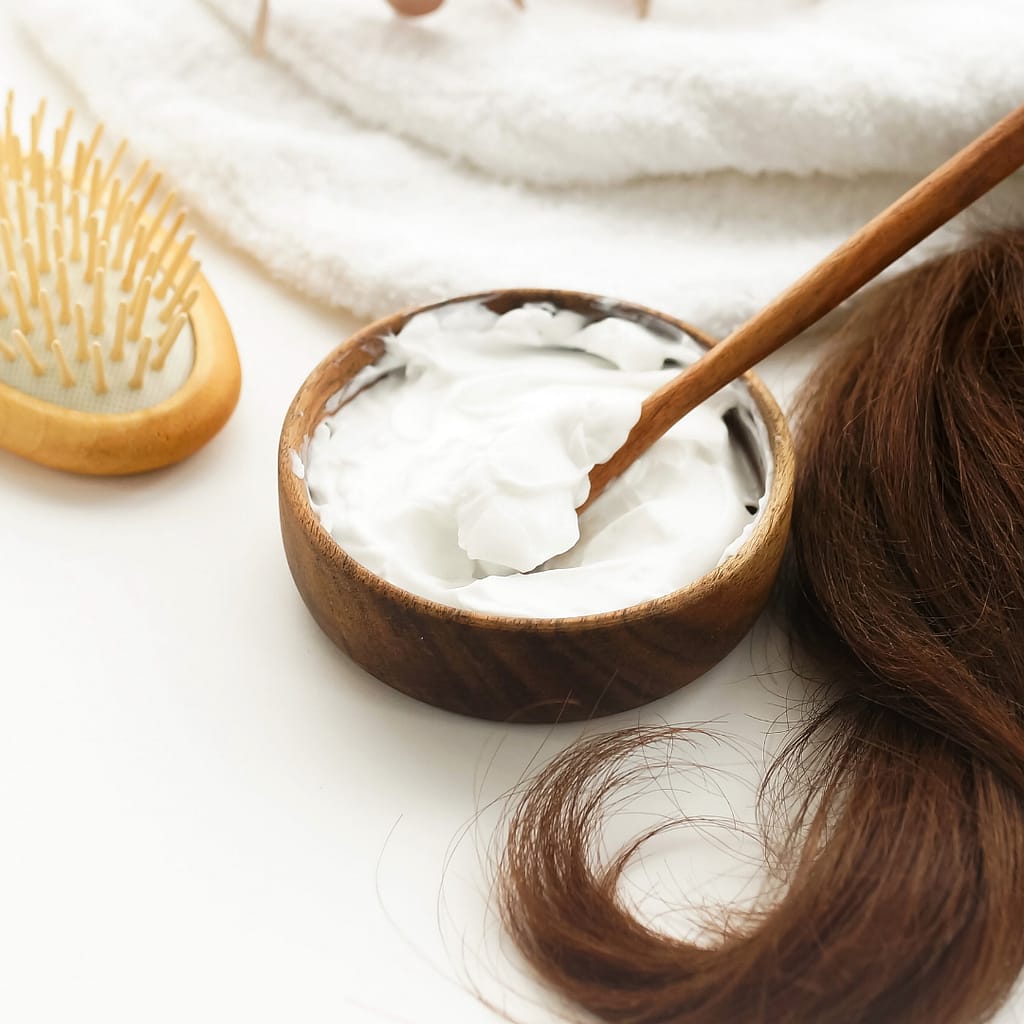 healthy hair oil mask mixed in wooden bowl with hair extensions laying beside it with a hair brush