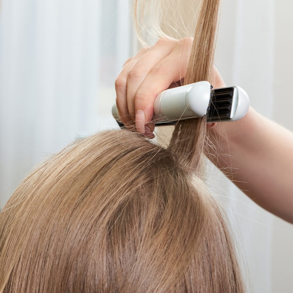 Close-up of a hair crimper tool in use, creating textured waves on blonde hair