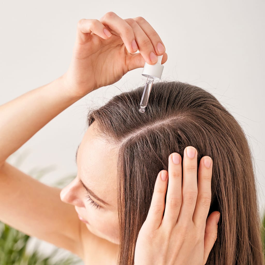 A woman applying rosemary oil to her scalp with a dropper, focusing on the benefits of using rosemary oil for promoting hair growth and scalp health.