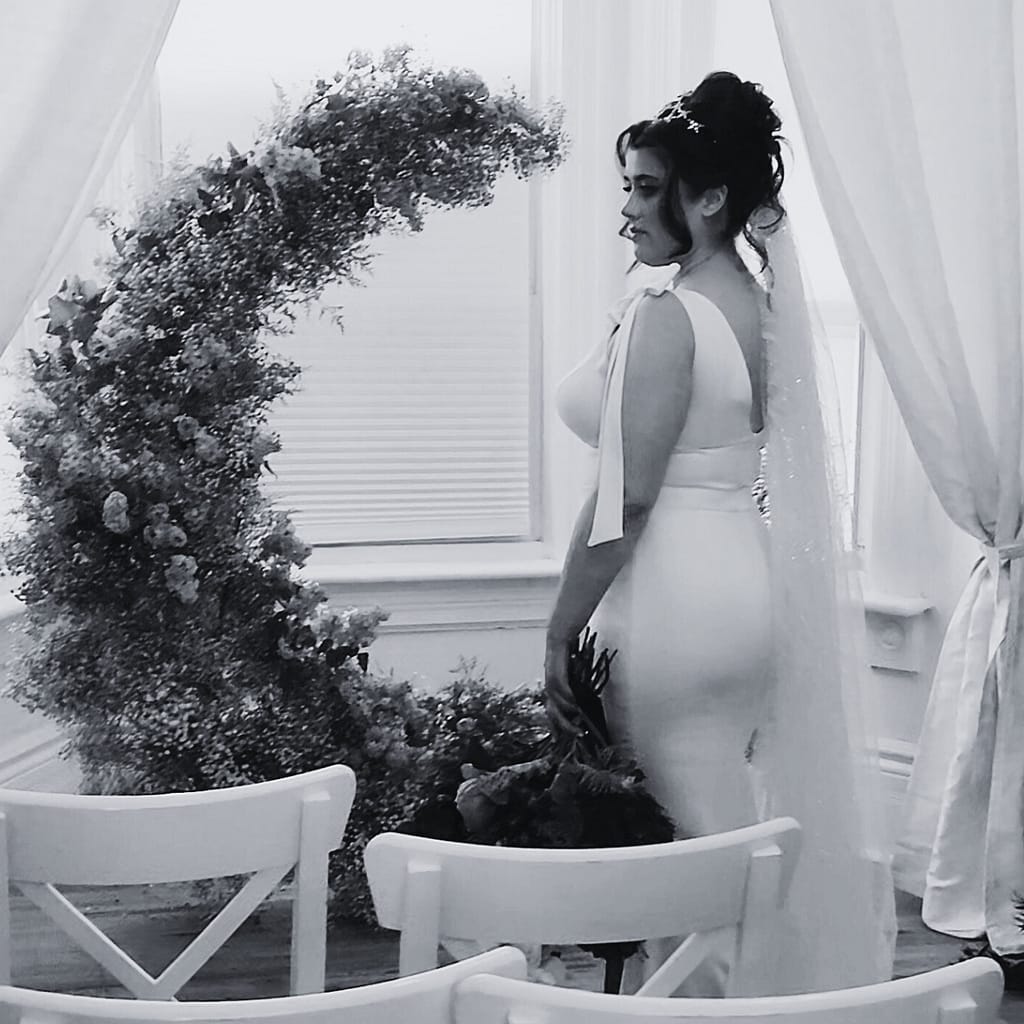 bride posing in front of a flower arch with wedding hair styled in an updo