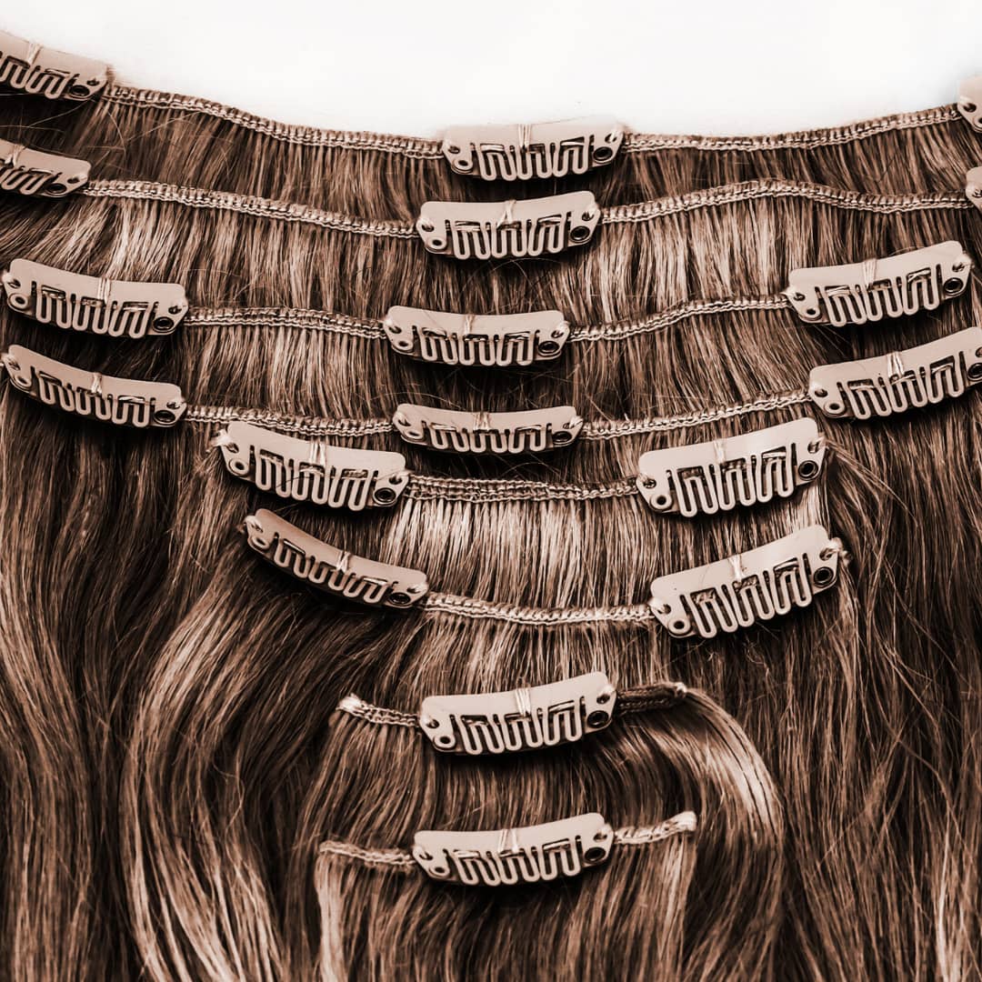 Close-up view of multiple brown clip-in hair extensions, showing the clips attached to the wefts, arranged in layers. The clips are metallic with a secure grip design, ideal for easy and safe attachment to natural hair.