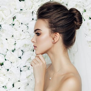 bride profile shot with bun wedding hairstyle in front of white rose wedding flower wall