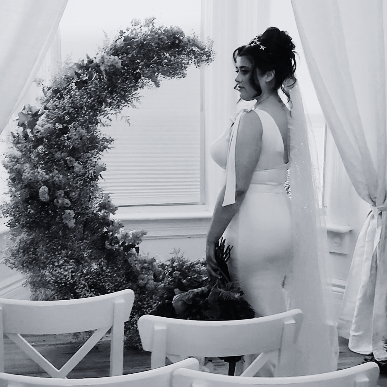 bride posing in front of a flower arch with wedding hair styled in an updo