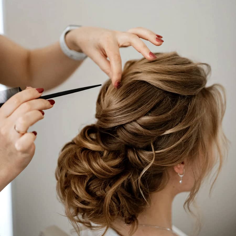 wedding hair updo low bun thick hair loose curls mobile hairstylist using hair comb to finish bridal hairstyle updo